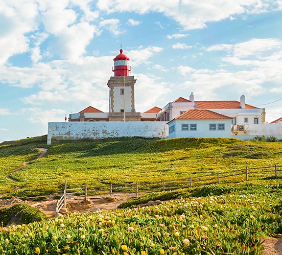 Cabo da Roca lighthouse with surrounding green landscape and blue sky.