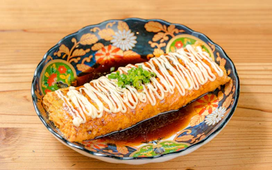 Tempeaki dish garnished with mayonnaise and green onions on a decorative plate.