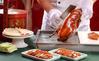 Chef preparing Peking duck with pancakes and vegetables in Beijing.