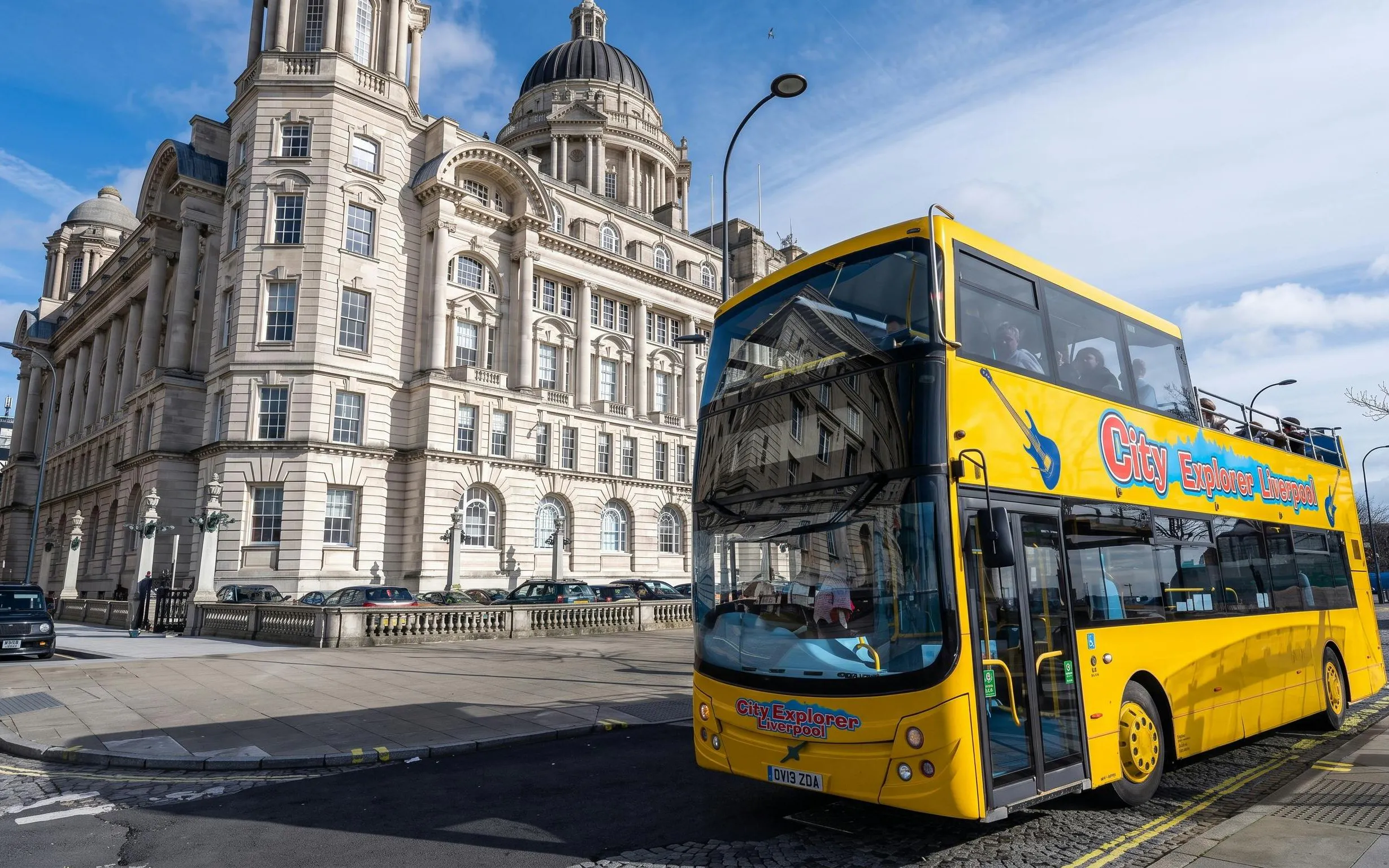 Yellow sightseeing bus in front of historic building in Liverpool.