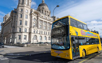 Yellow sightseeing bus in front of historic building in Liverpool.