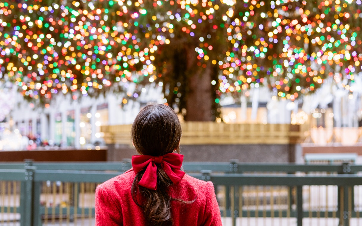 Person admiring holiday lights on a large Christmas tree at Rockefeller Center, New York City.