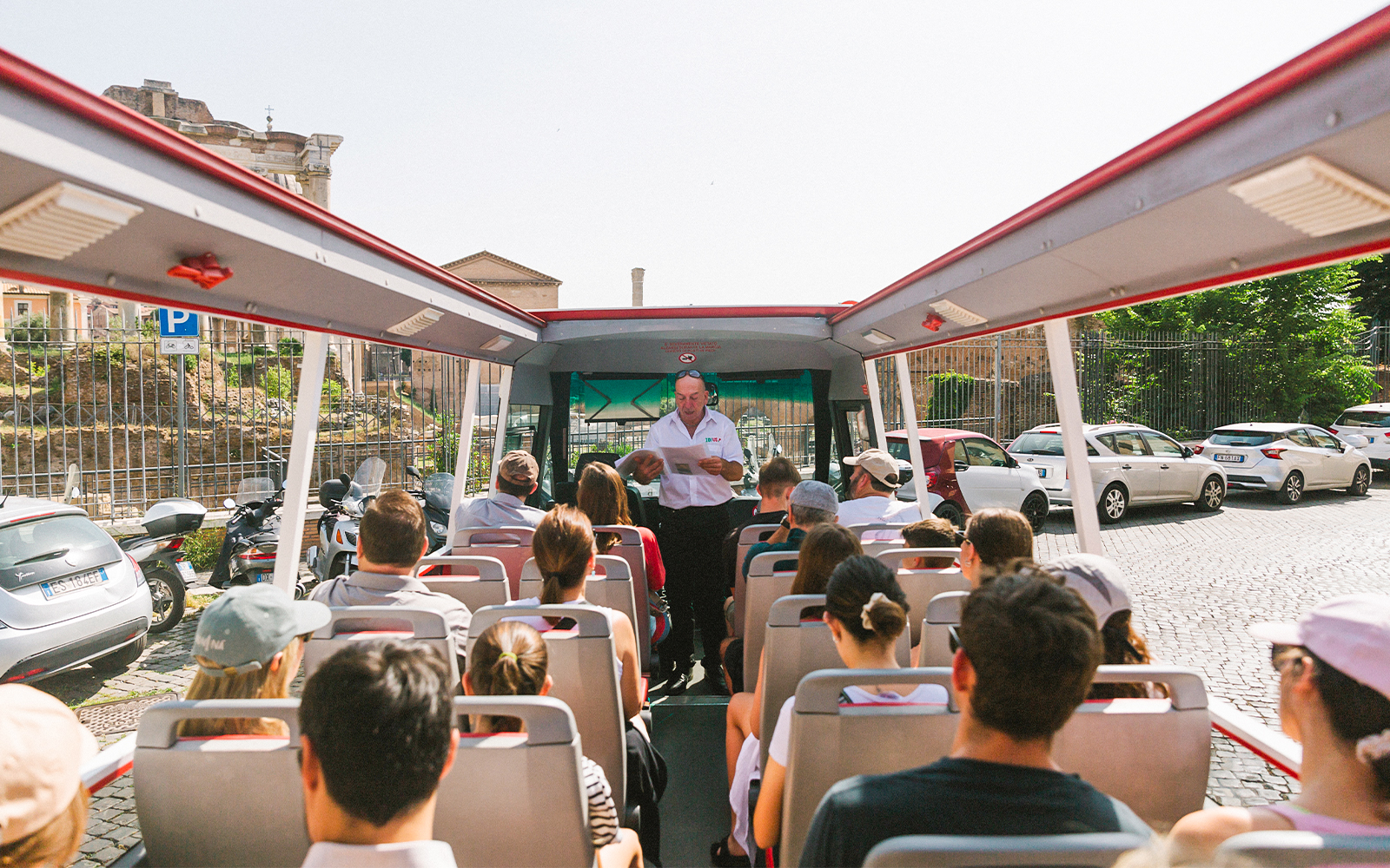 Tour group on open-top bus near Capuchin Crypt, Rome, with guide providing audio information.