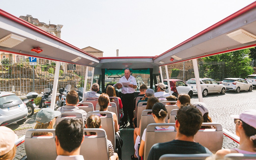 Tour group on open-top bus near Capuchin Crypt, Rome, with guide providing audio information.