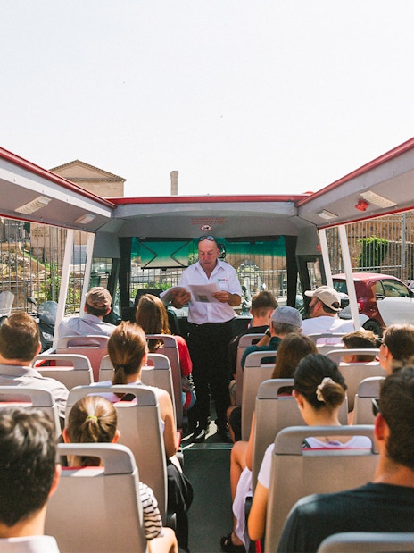 Tour group on open-top bus near Capuchin Crypt, Rome, with guide providing audio information.