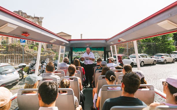 Tour group on open-top bus near Capuchin Crypt, Rome, with guide providing audio information.