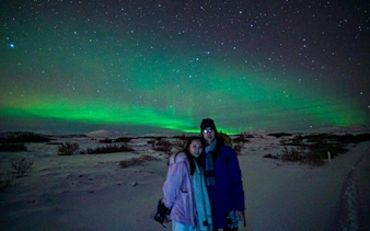 Northern Lights over snowy landscape with two people on a Reykjavik jeep tour.