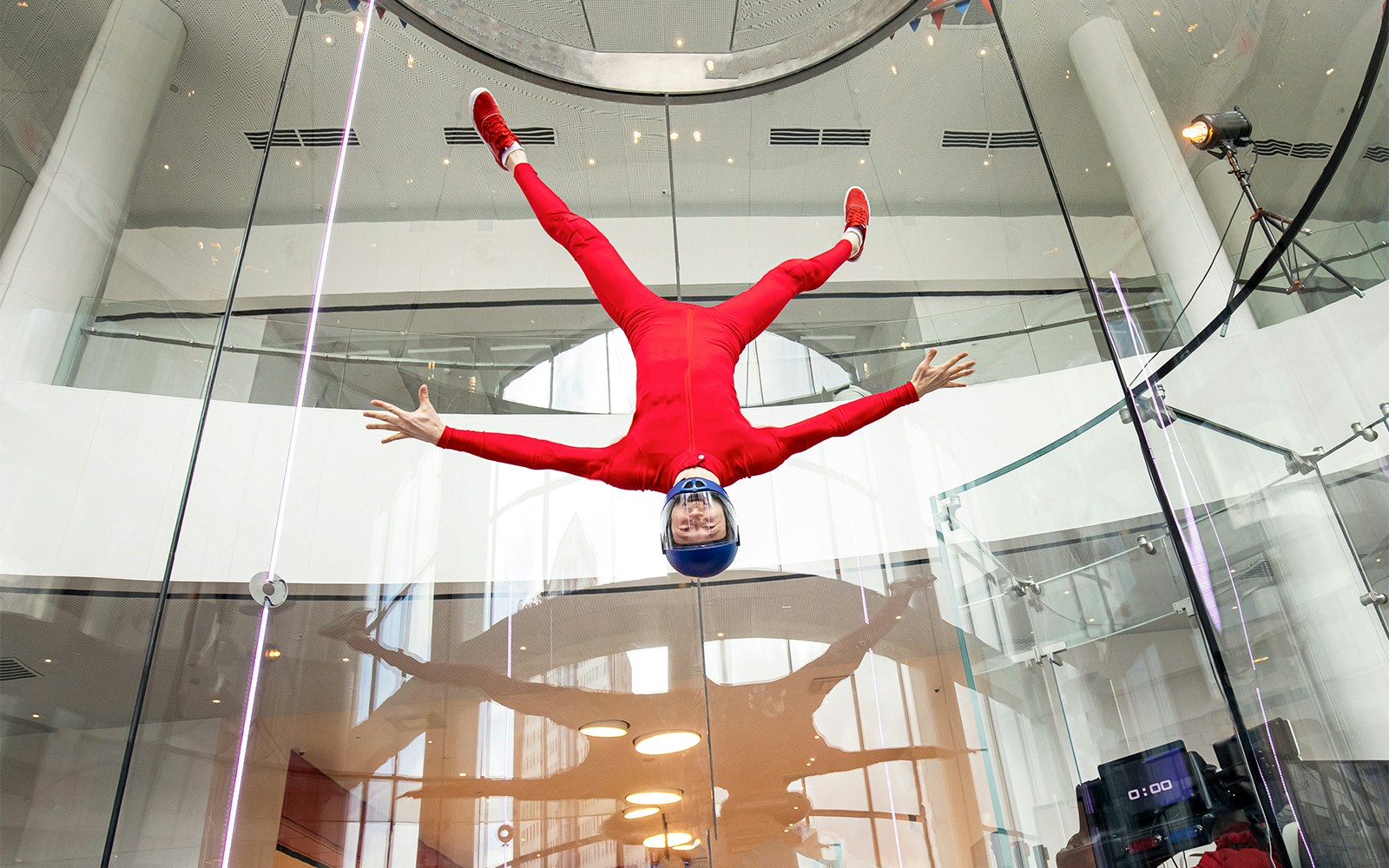 Skydiver in red suit floating upside down at iFly Singapore wind tunnel.
