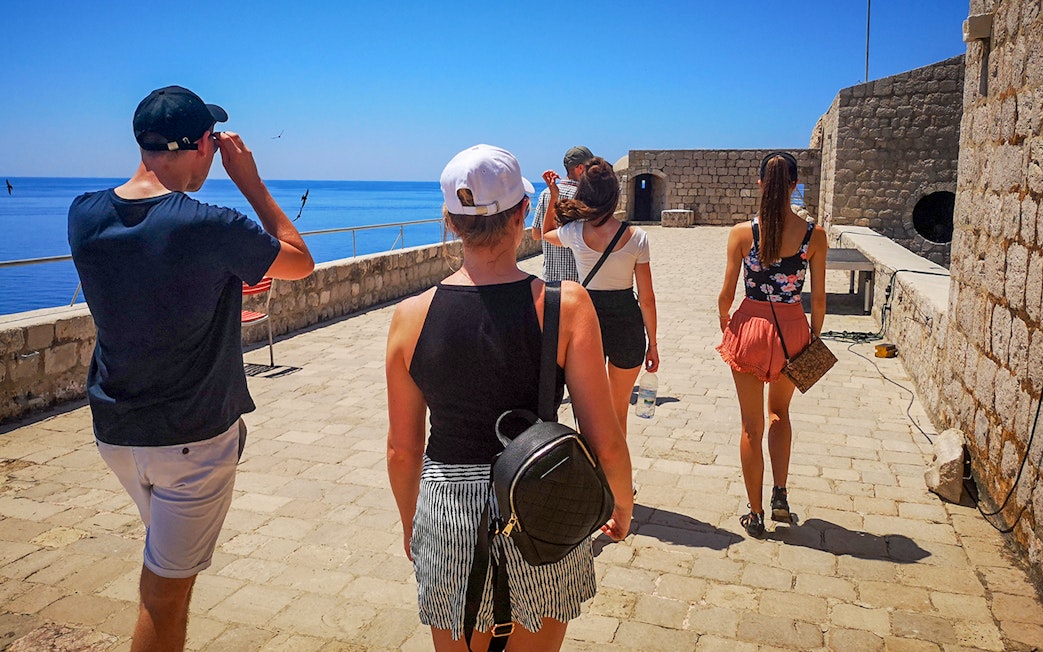 Guests walking along the stone pathway of Lovrijenac Fort, overlooking the sea.