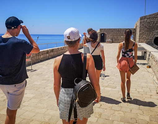 Guests walking along the stone pathway of Lovrijenac Fort, overlooking the sea.
