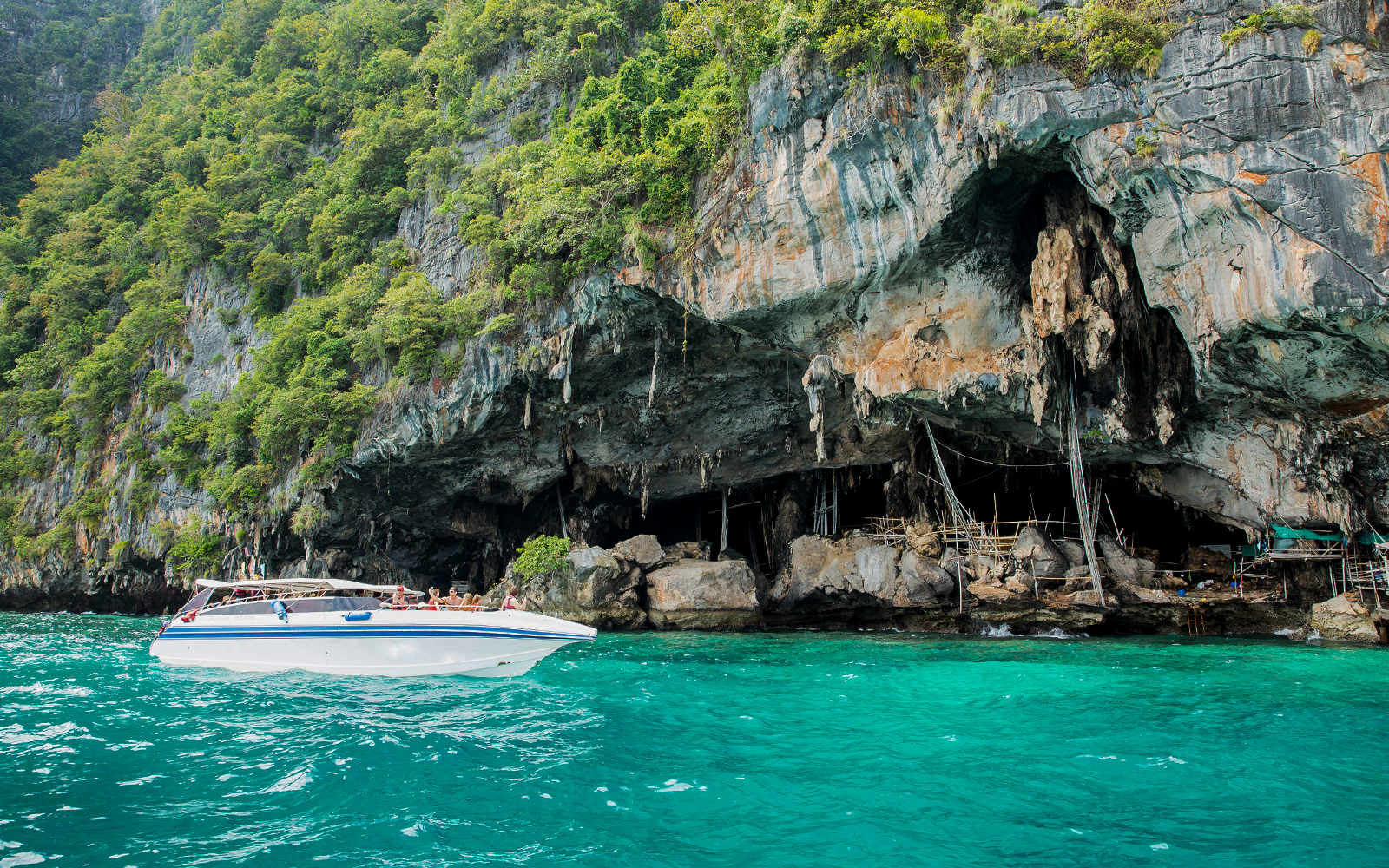 Speedboat near Viking Cave on Phi Phi Island, Thailand, with lush cliffs and turquoise water.