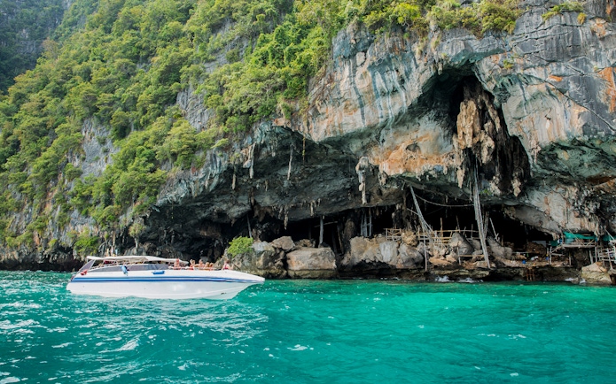 Speedboat near Viking Cave on Phi Phi Island, Thailand, with lush cliffs and turquoise water.