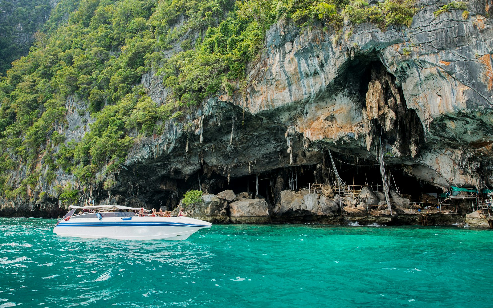 Speedboat near Viking Cave on Phi Phi Island, Thailand, with lush cliffs and turquoise water.