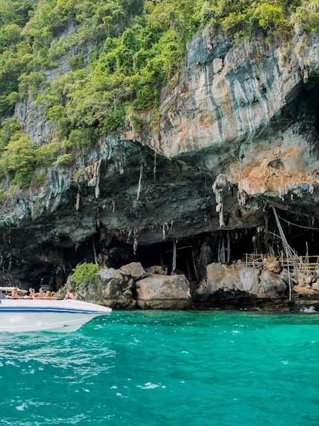 Speedboat near Viking Cave on Phi Phi Island, Thailand, with lush cliffs and turquoise water.