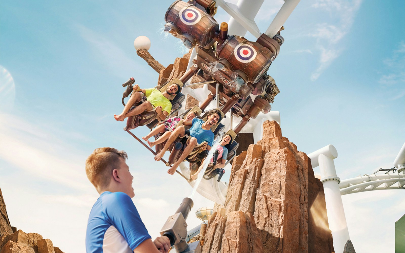 Visitors enjoying a ride at Bandit Zone, Yas Waterworld, with water cannons and rocky backdrop.