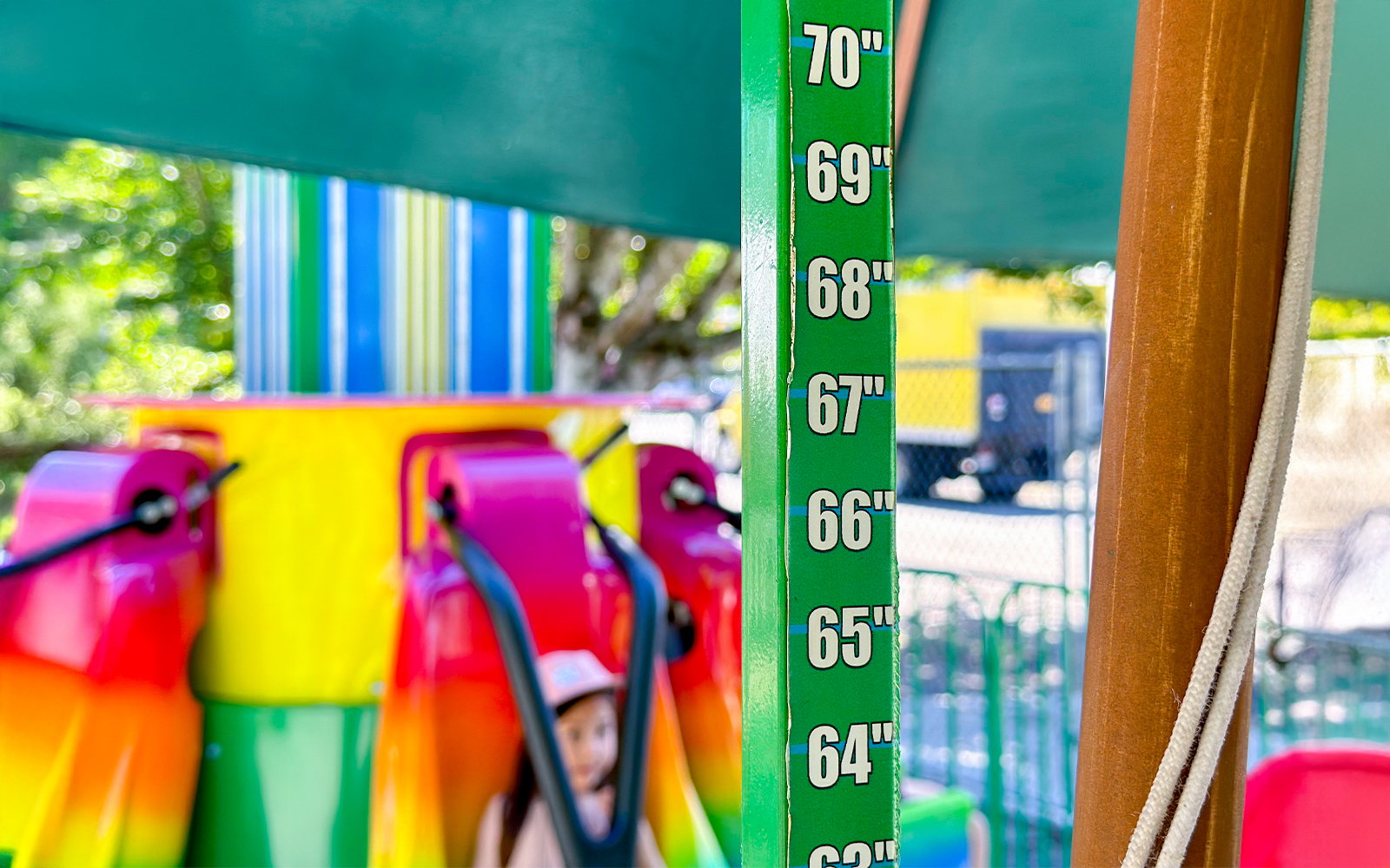 Height ruler at ride entrance with colorful seats in background.