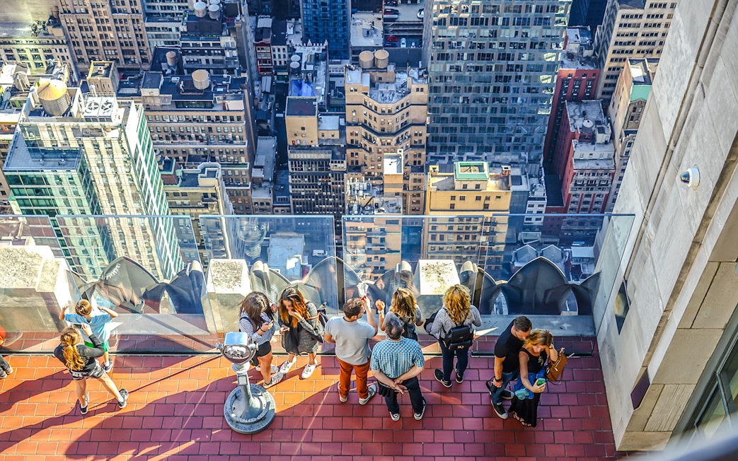 Visitors on the observation deck at Rockefeller Center overlooking New York City buildings.