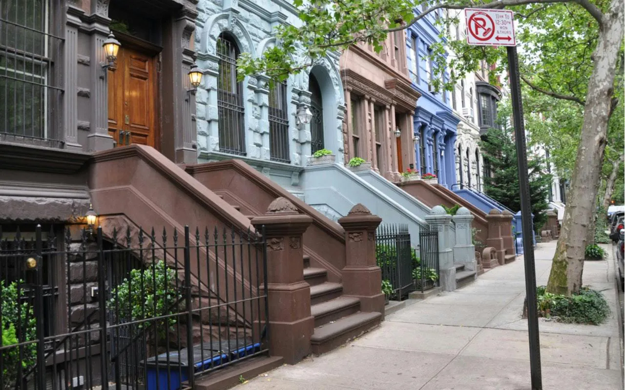 Brownstone buildings on a tree-lined street in Manhattan, part of a self-guided exploration game in New York.