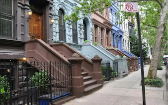 Brownstone buildings on a tree-lined street in Manhattan, part of a self-guided exploration game in New York.