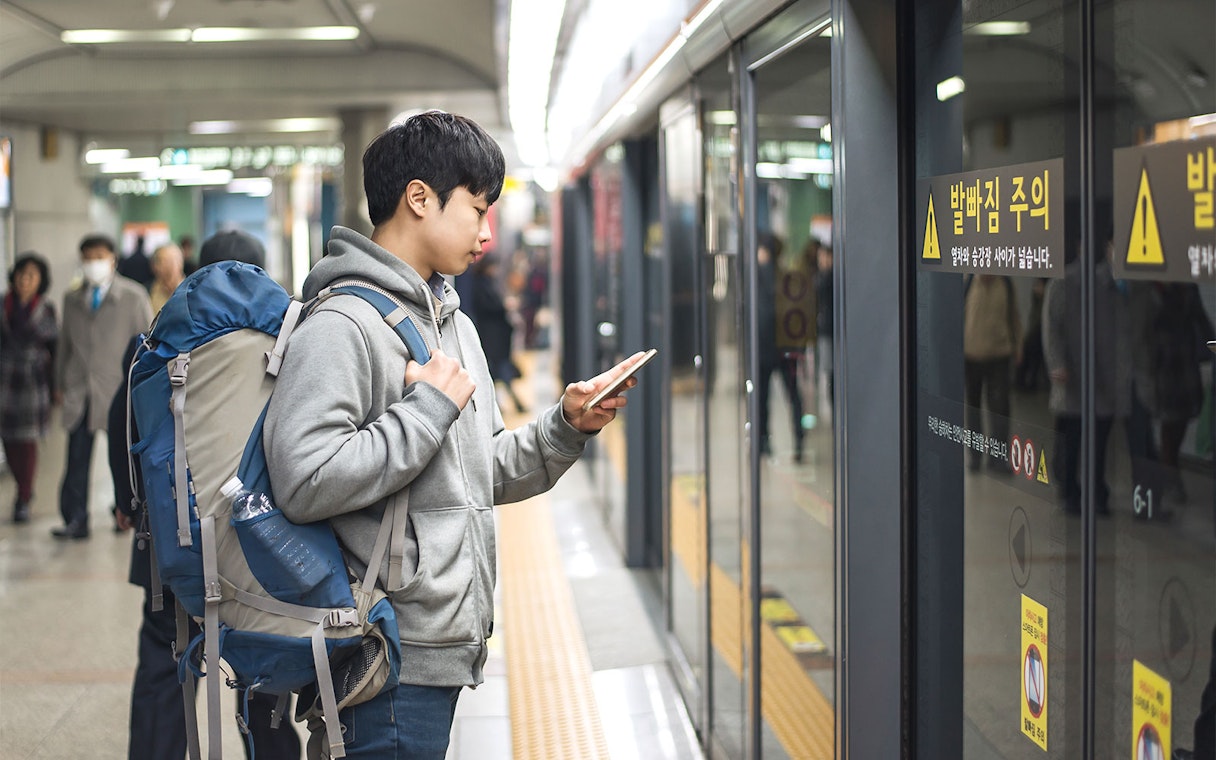 Traveler with backpack using phone at subway station in Korea.