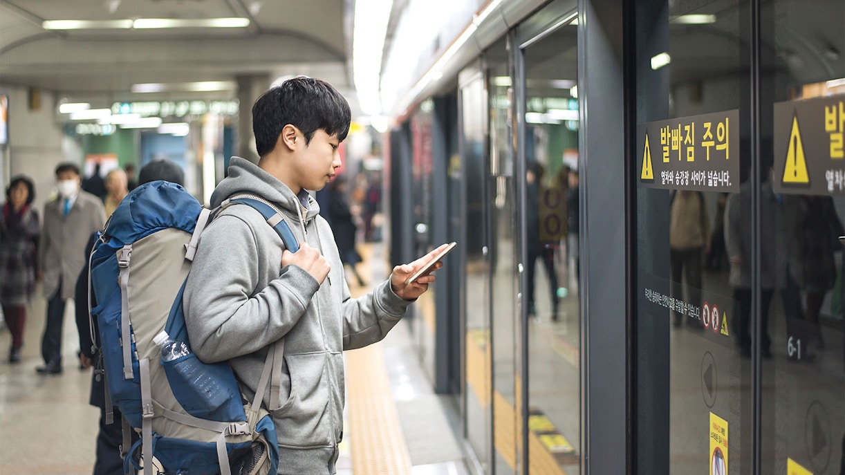 Traveler with backpack using phone at subway station in Korea.