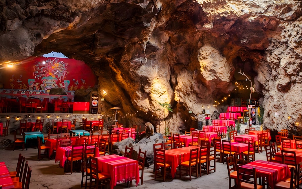 Dining area inside La Cueva Teotihuacán restaurant with cave walls and colorful tables.