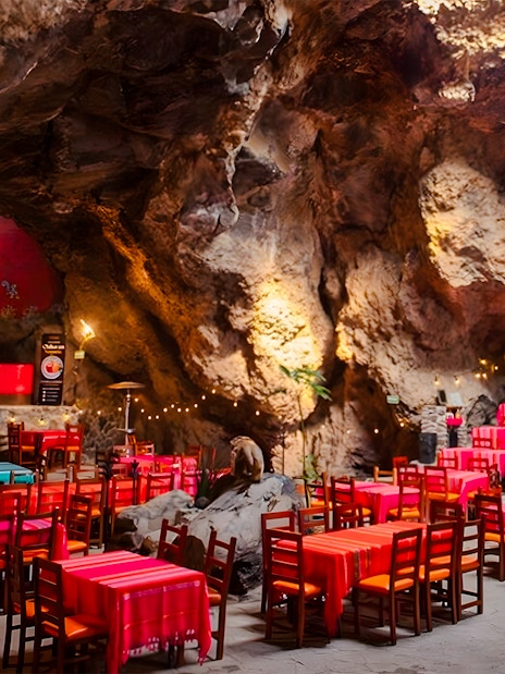 Dining area inside La Cueva Teotihuacán restaurant with cave walls and colorful tables.