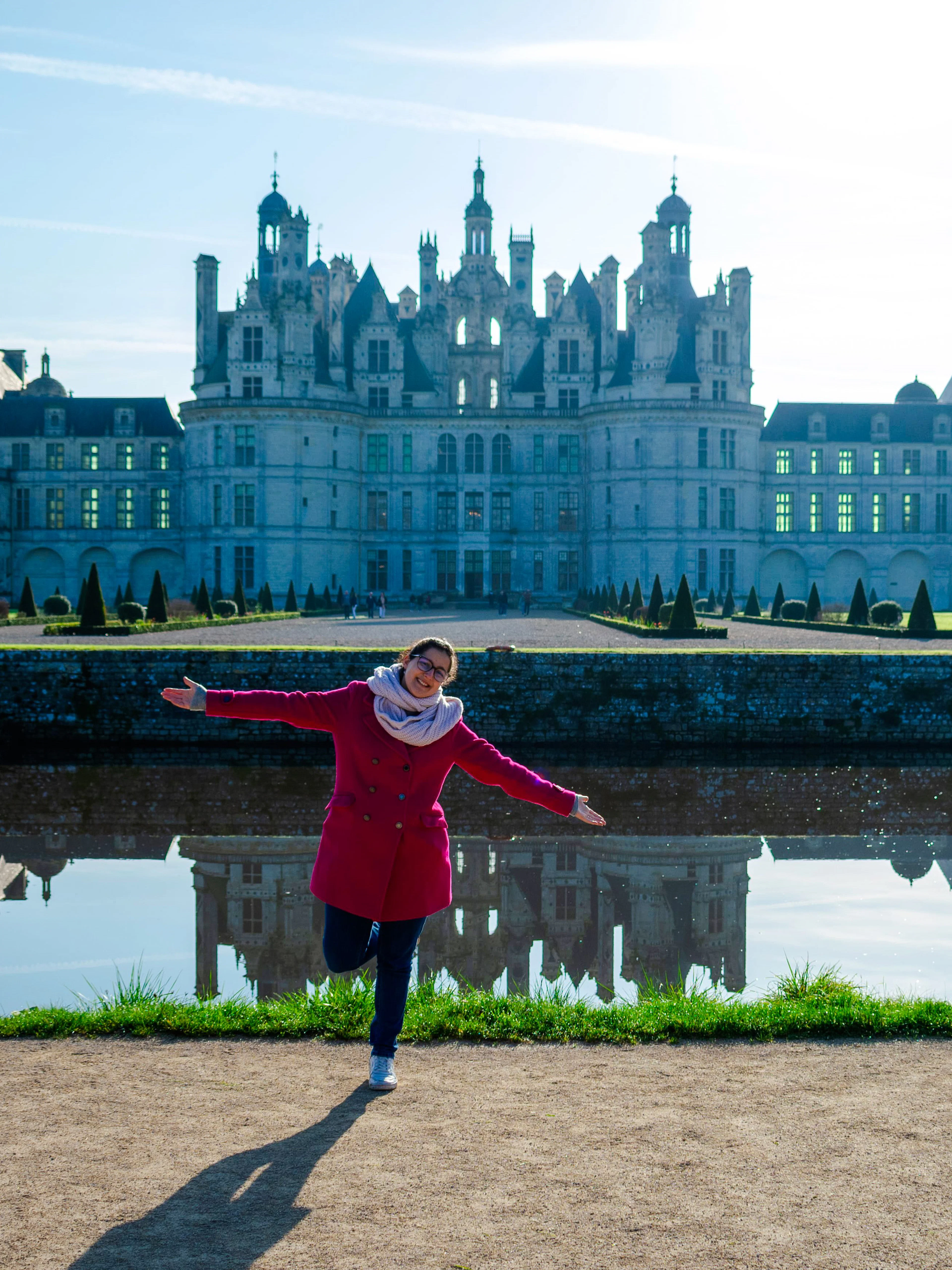 Person posing in front of Chambord Castle with reflection in water, France.