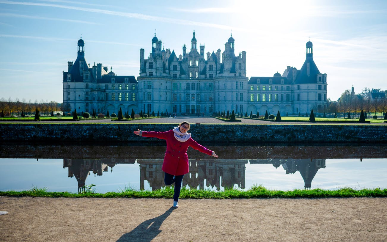 Person posing in front of Chambord Castle with reflection in water, France.