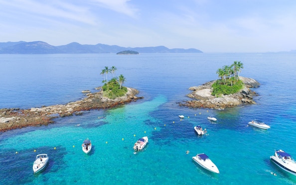 Boats near Ilha Botinas in Angra dos Reis, Rio de Janeiro, with clear blue water and small islands.