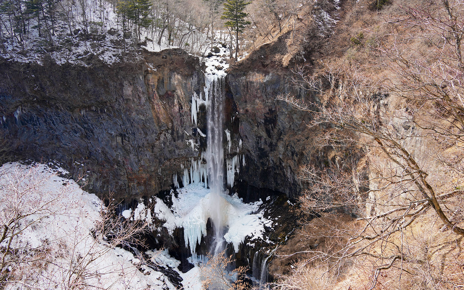Kegon Falls in Nikkō National Park, surrounded by snow-covered cliffs and bare trees.