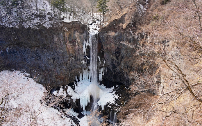 Kegon Falls in Nikkō National Park, surrounded by snow-covered cliffs and bare trees.