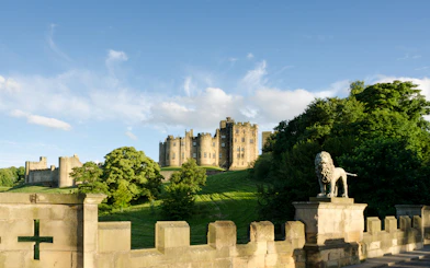 Alnwick Castle viewed from Lion Bridge with stone lion statue in foreground.
