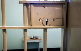 Robben Island Prison cell door lock with a metal bed and dish in the background.