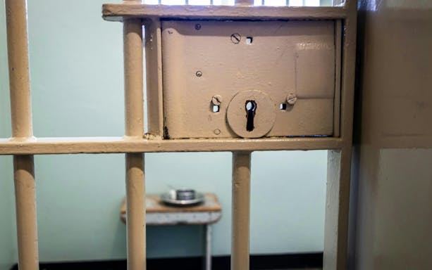 Robben Island Prison cell door lock with a metal bed and dish in the background.