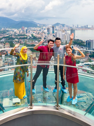 Visitors on a glass skywalk with a view of Penang cityscape in Malaysia.