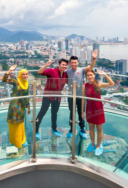 Visitors on a glass skywalk with a view of Penang cityscape in Malaysia.