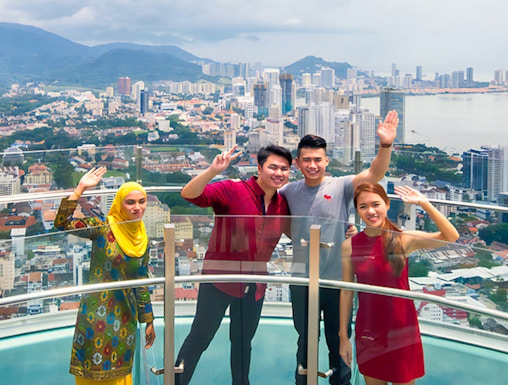 Visitors on a glass skywalk with a view of Penang cityscape in Malaysia.