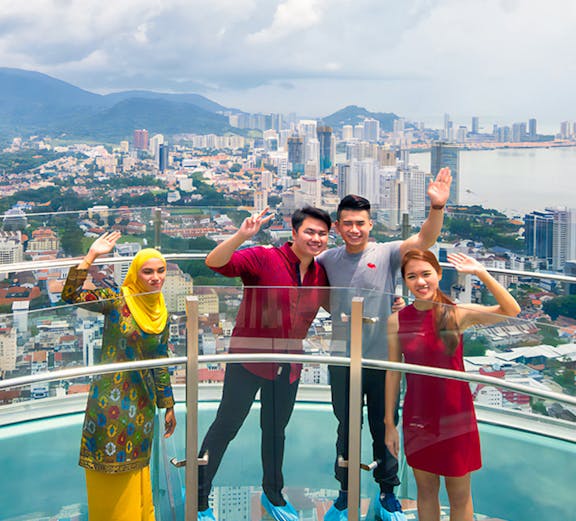 Visitors on a glass skywalk with a view of Penang cityscape in Malaysia.