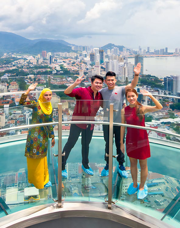 Visitors on a glass skywalk with a view of Penang cityscape in Malaysia.