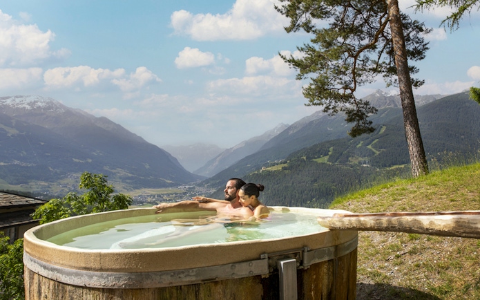 Couple relaxing in an outdoor hot tub with mountain views at QC Terme Bagni Vecchi di Bormio.