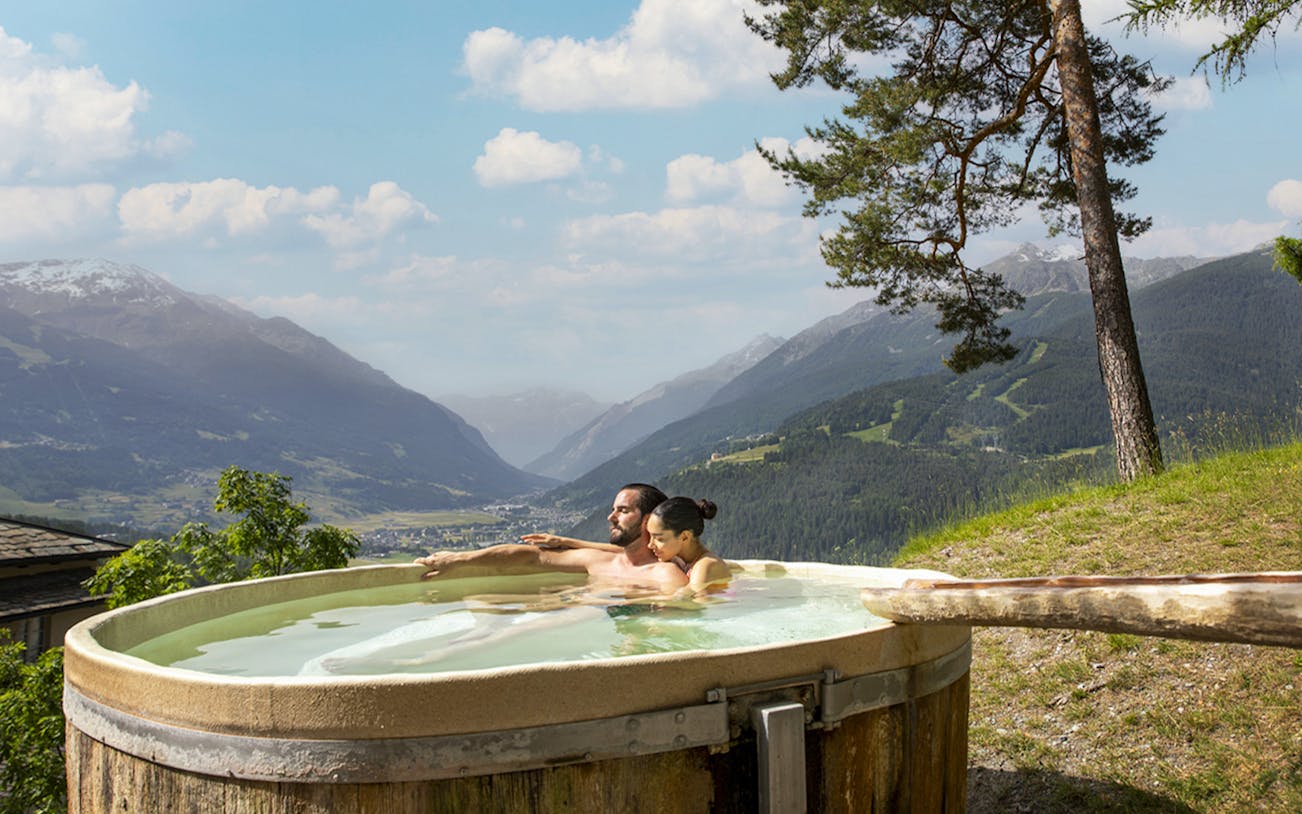 Couple relaxing in an outdoor hot tub with mountain views at QC Terme Bagni Vecchi di Bormio.