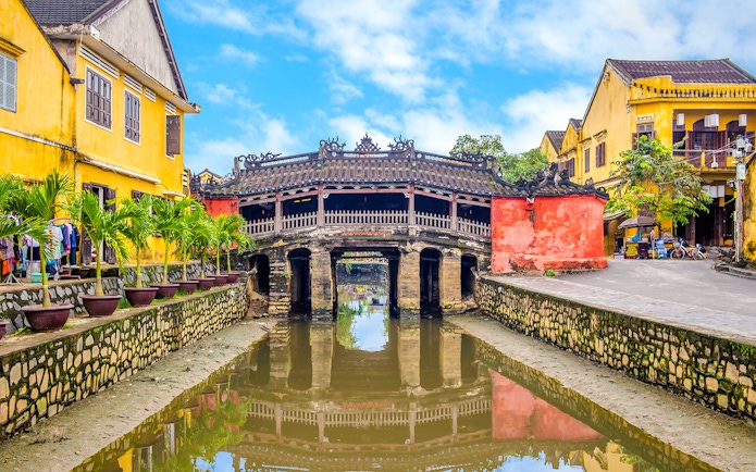 Japanese Bridge in Hoi An with yellow buildings and water reflection.