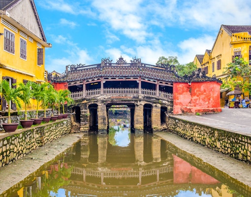 Japanese Bridge in Hoi An with yellow buildings and water reflection.