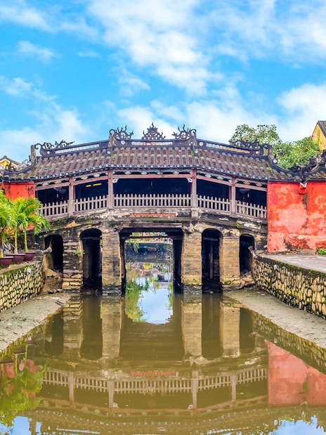 Japanese Bridge in Hoi An with yellow buildings and water reflection.
