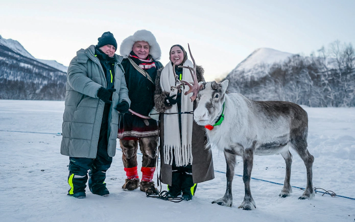 Guests with a reindeer during a Sámi culture experience in snowy landscape.