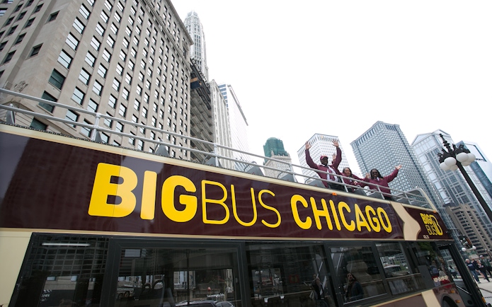 Open-top bus with tourists on Chicago Hop-On-Hop-Off Tour, skyscrapers in background.