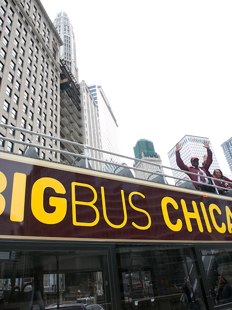 Open-top bus with tourists on Chicago Hop-On-Hop-Off Tour, skyscrapers in background.