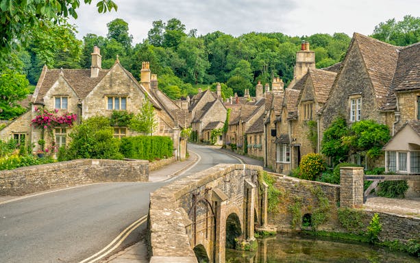 Stone cottages and bridge in a Cotswolds village, surrounded by greenery.