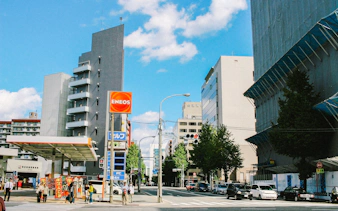 ENEOS gas station on a city street with surrounding buildings and pedestrians.